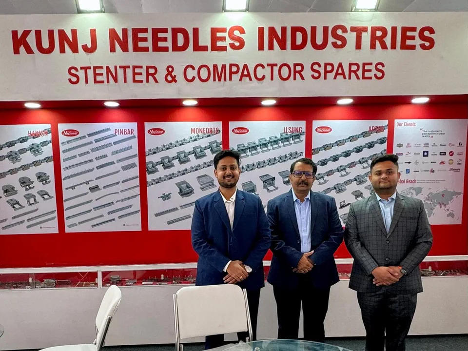 Three people standing at a manufacturing trade-show display for textile-machine spares